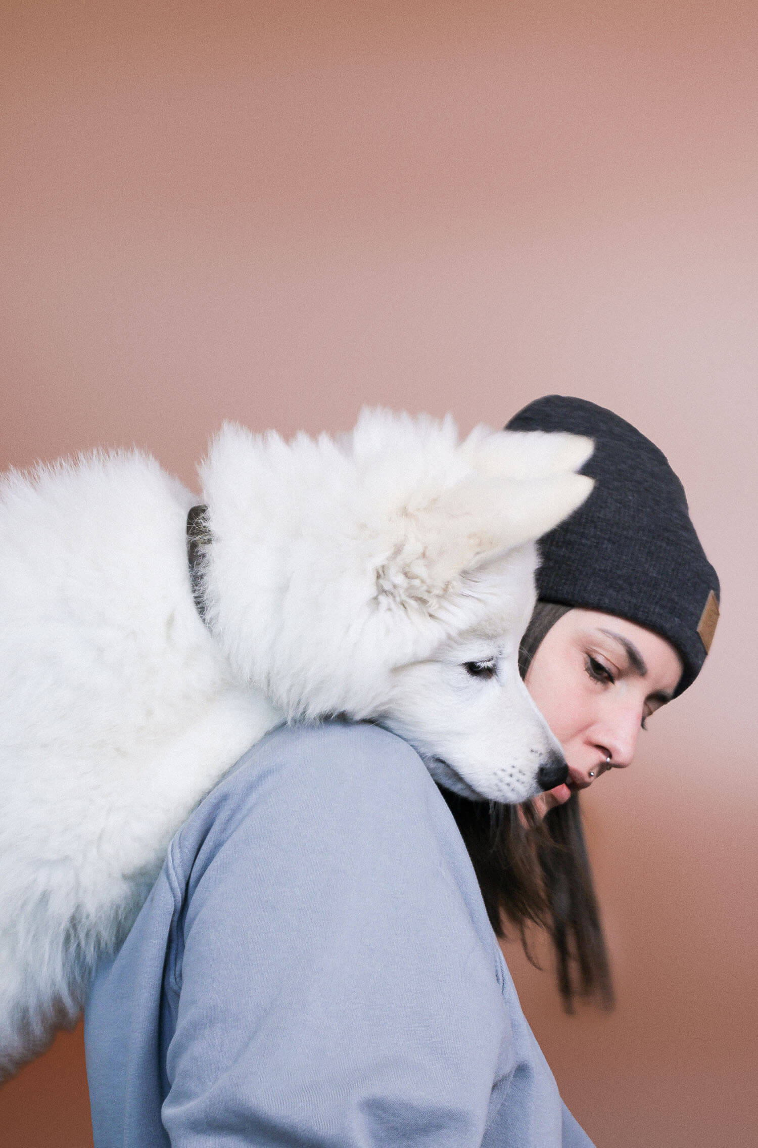 kerstin dörflinger und ihr weißer schäferhund. der hund schaut kerstin über die schulter, sie sitzt vor einem braunen hintergrund.